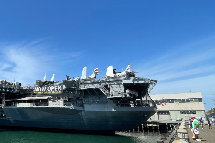 a large ship in a body of water with USS Midway Museum in the background