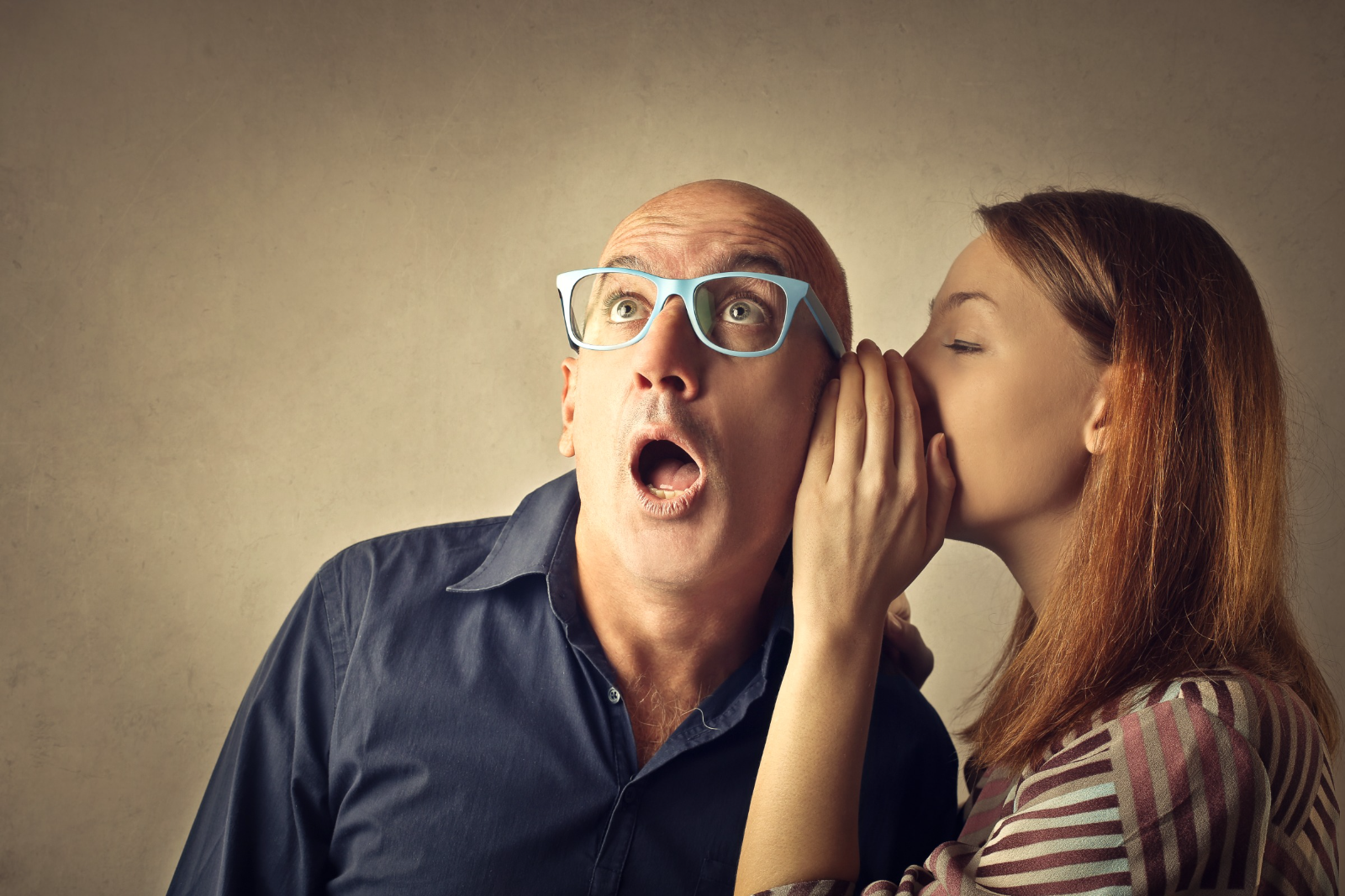 a man wearing glasses being told a secret