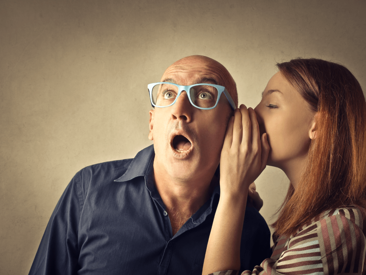 a man wearing glasses being told a secret
